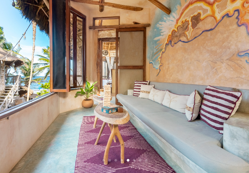 Balcony with a gray couch, purple rug, wooden table, and ocean view.