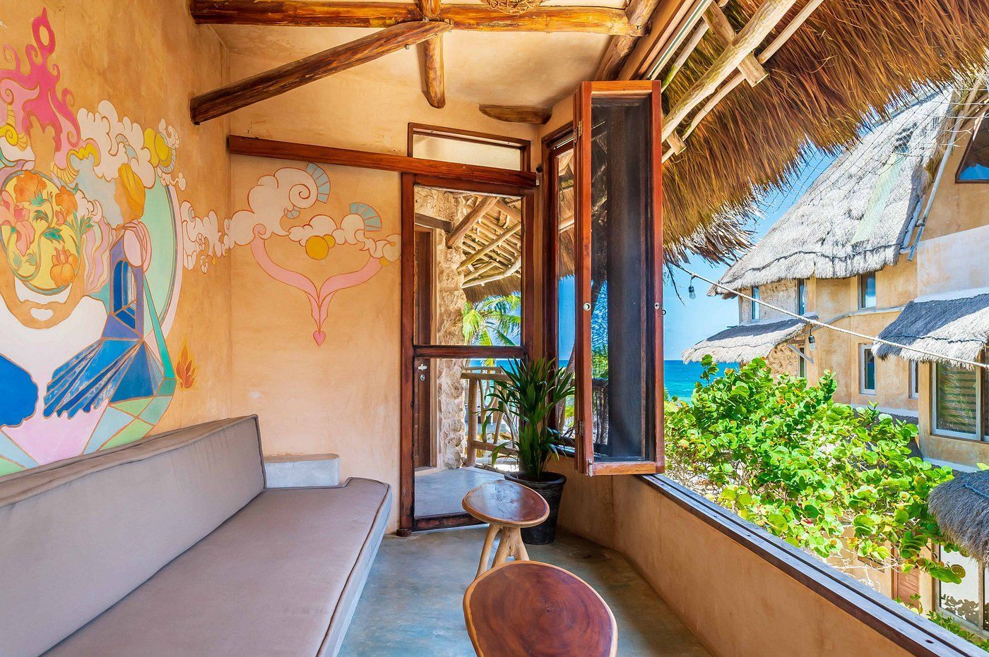 Balcony with a tan couch, wooden furniture, and ocean view; painted wall art.