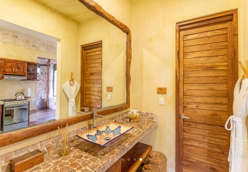 Bathroom with decorative sink, large mirror, wooden door, and stone countertop.