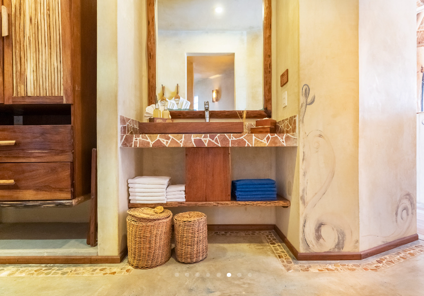Bathroom with wooden vanity, mirror, shelf, towels, and decorative baskets.