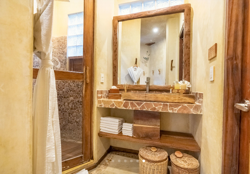 Bathroom with wooden vanity, mirror, and a stone sink. Neutral colors, natural materials, and shower visible.