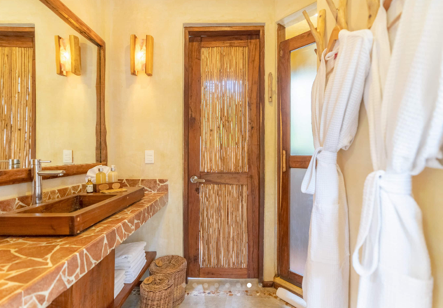 Bathroom with wooden door, sink, and decorative lighting. White robes hang on a wall.