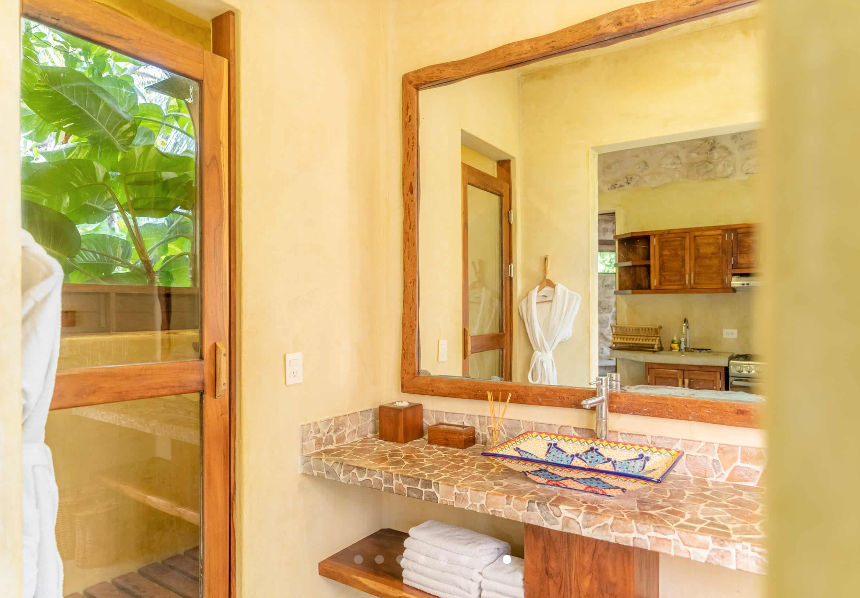 Bathroom with mirror, counter, and sink. Wooden accents and outdoor view.