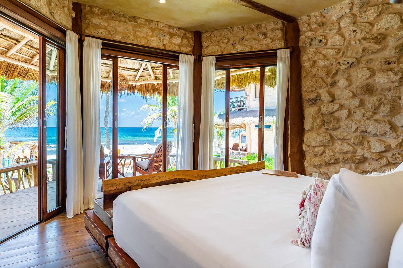 Bedroom with bed, stone wall, ocean view through windows, and sliding door to balcony.