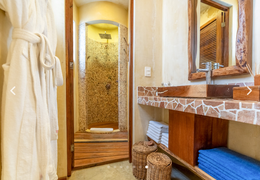 Bathroom with shower, vanity, and a robe. The shower has stone tile, and the vanity has a stone top.