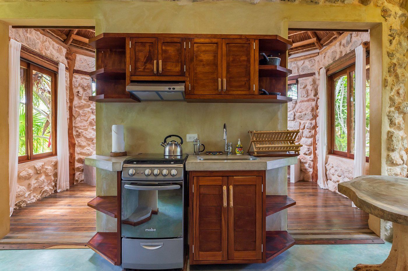 Kitchen with wooden cabinets, stove, and sink set into a stone wall. Two doorways lead to other rooms.