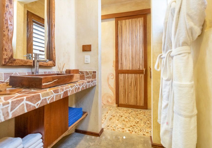 Bathroom with wooden sink, mirror, and door; patterned countertop, blue towels, white robe.