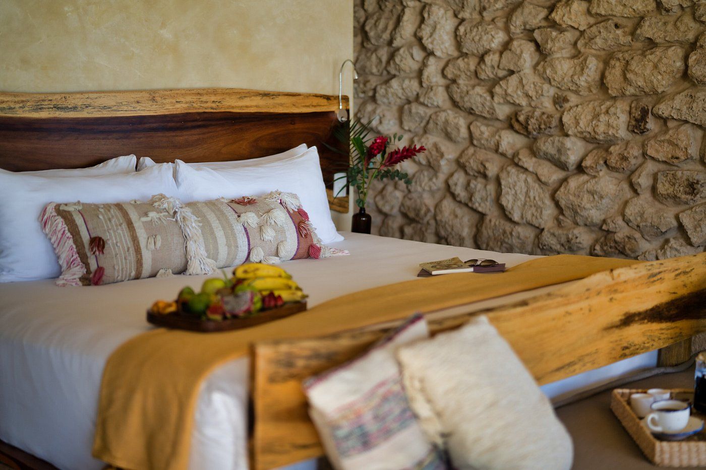 Bedroom with bed, fruit tray, rustic wooden headboard, and stone wall.