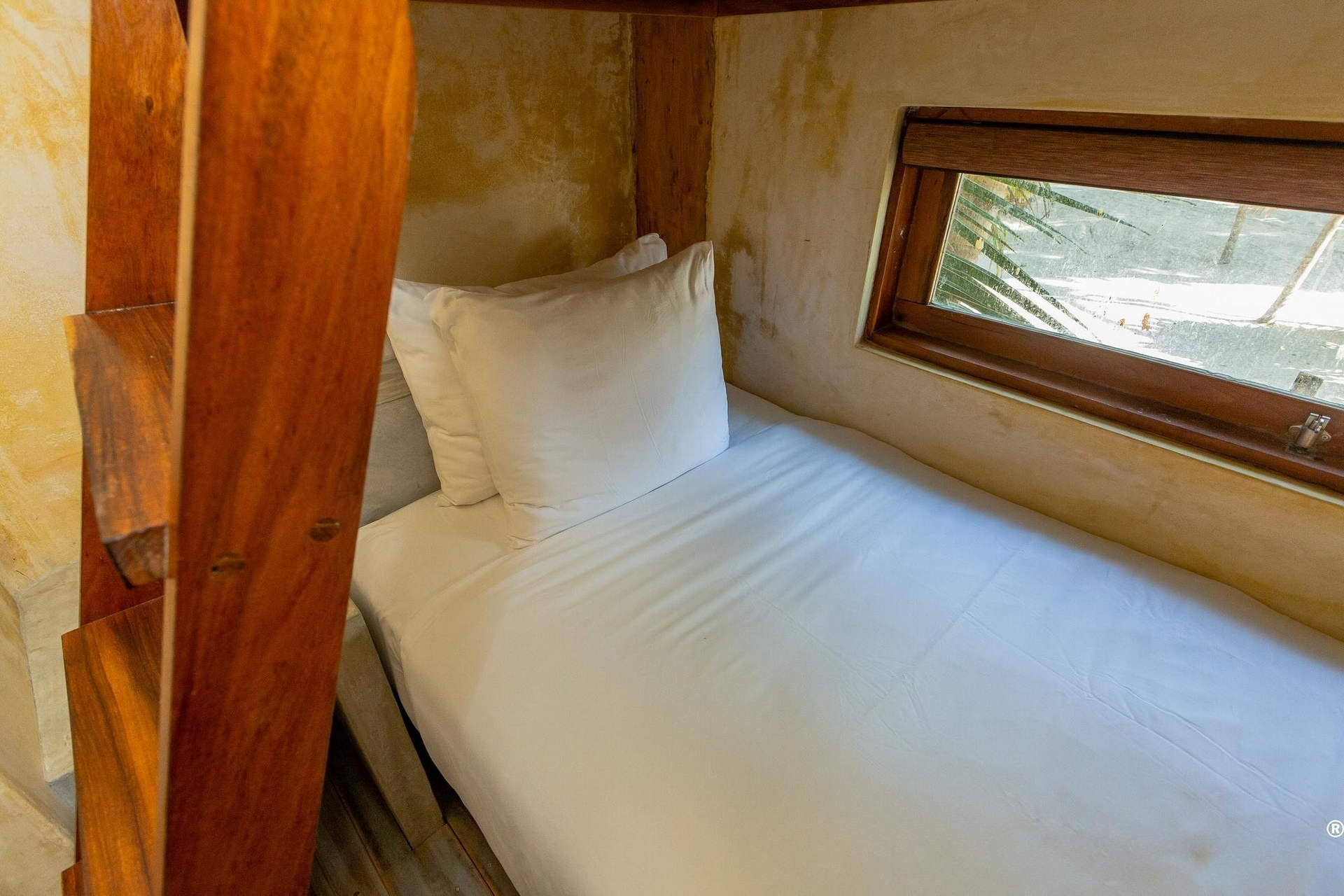Wooden bunk bed with a single, made bed next to a small window.