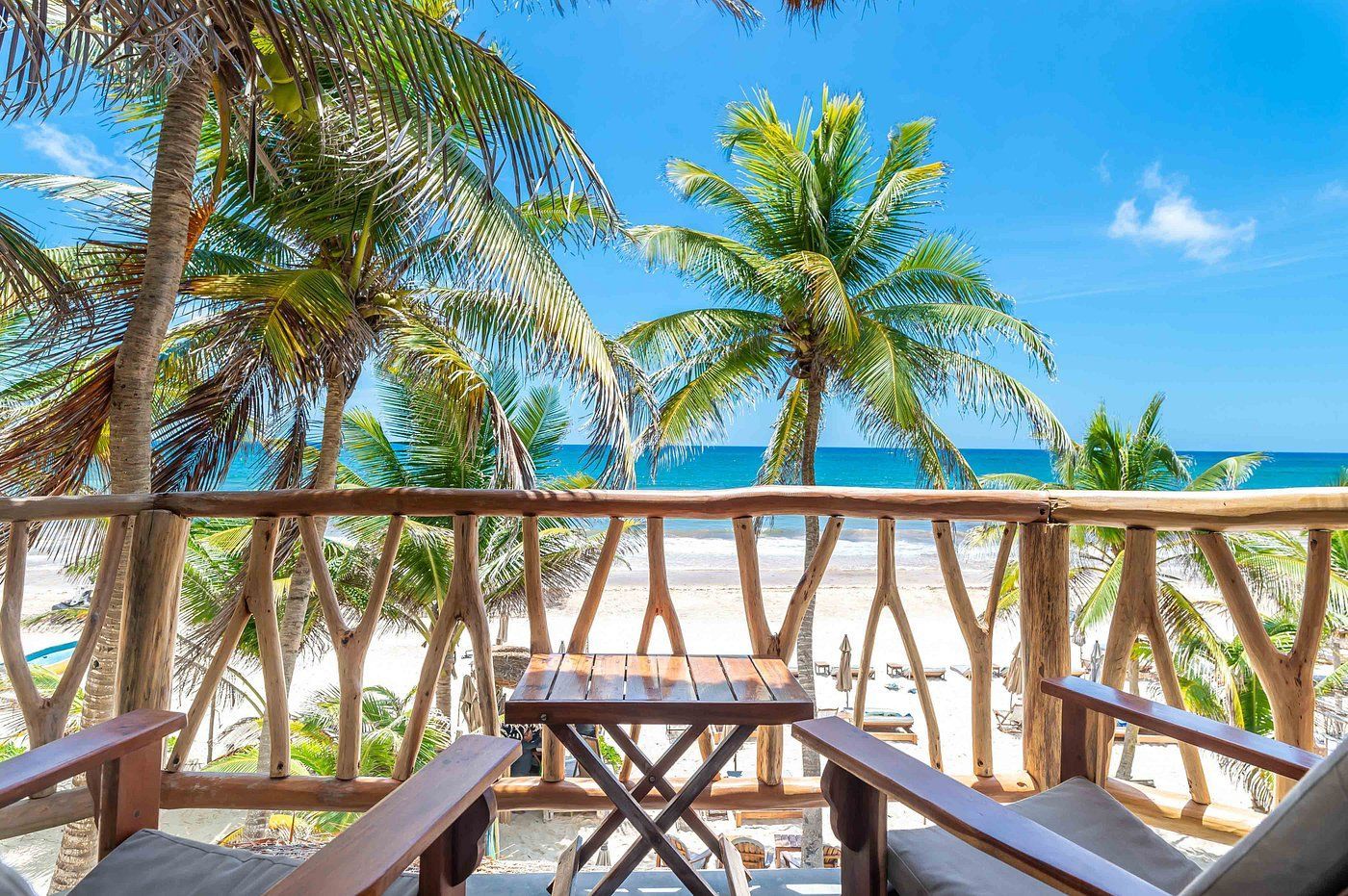 Balcony view of beach, palm trees, ocean, blue sky, two chairs, small table.