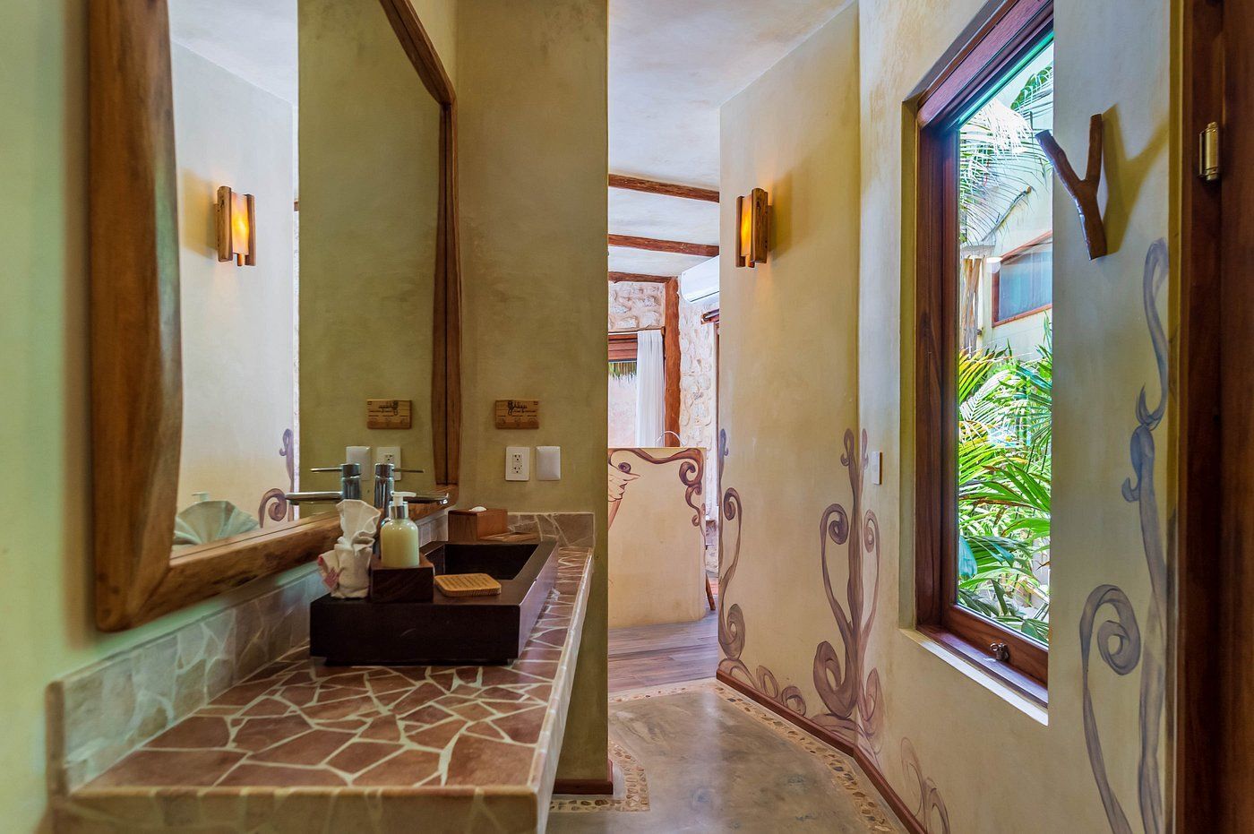Bathroom with a mosaic countertop, large mirror, and a window overlooking greenery. Decorative wall accents.