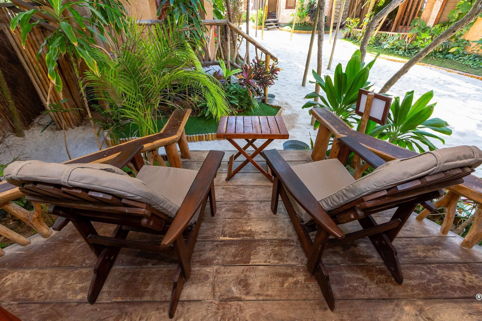 Two wooden chairs and a small table on a wooden deck in a tropical outdoor setting.