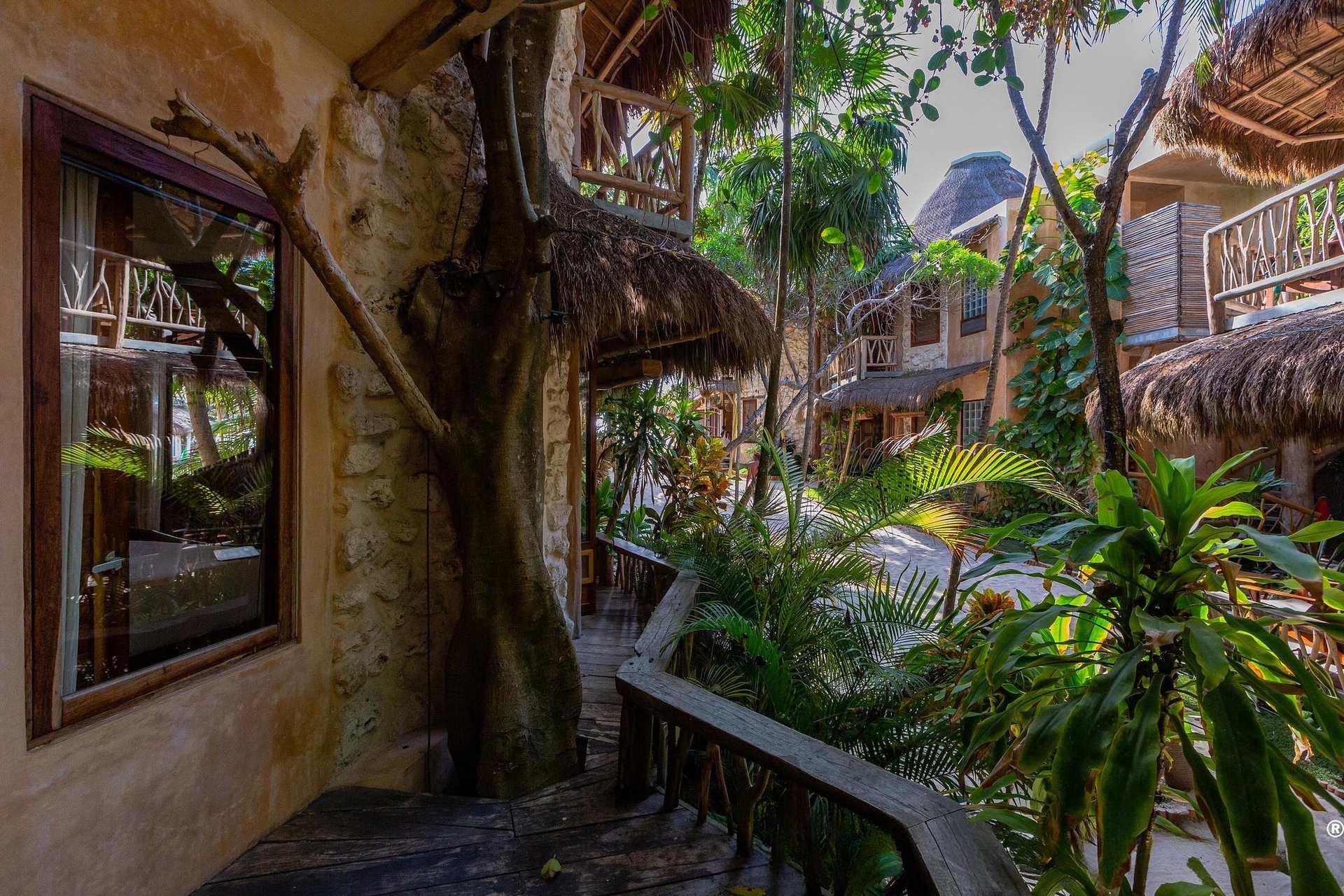 Exterior view of a tropical resort with a stone facade, thatched roofs, and lush greenery.