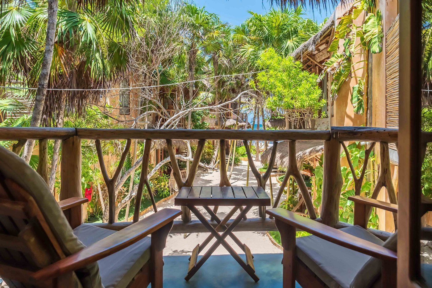 Balcony with wooden railing, chairs, and table overlooking lush green foliage.
