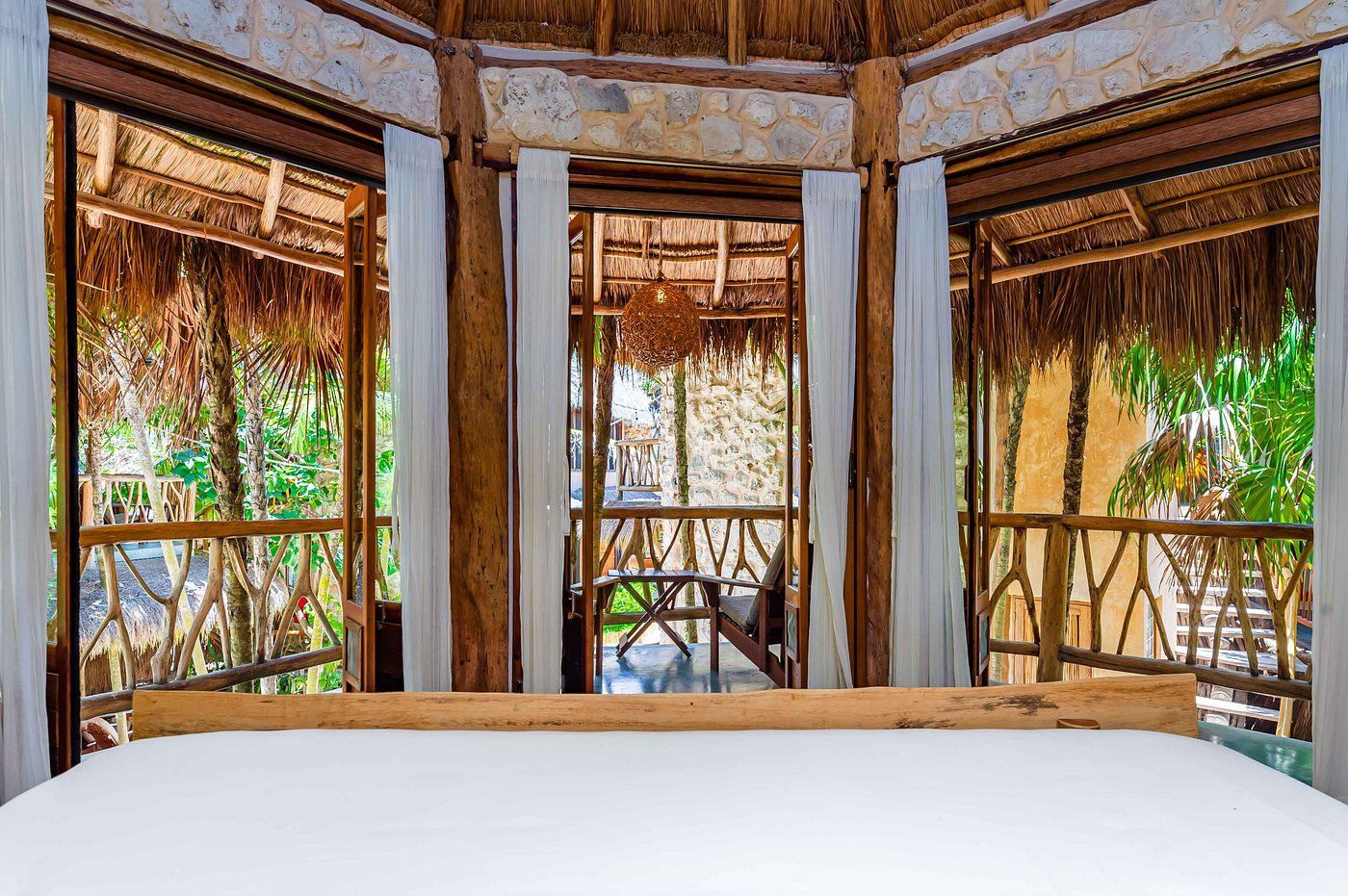Bedroom with bed, thatched roof, and views of greenery.
