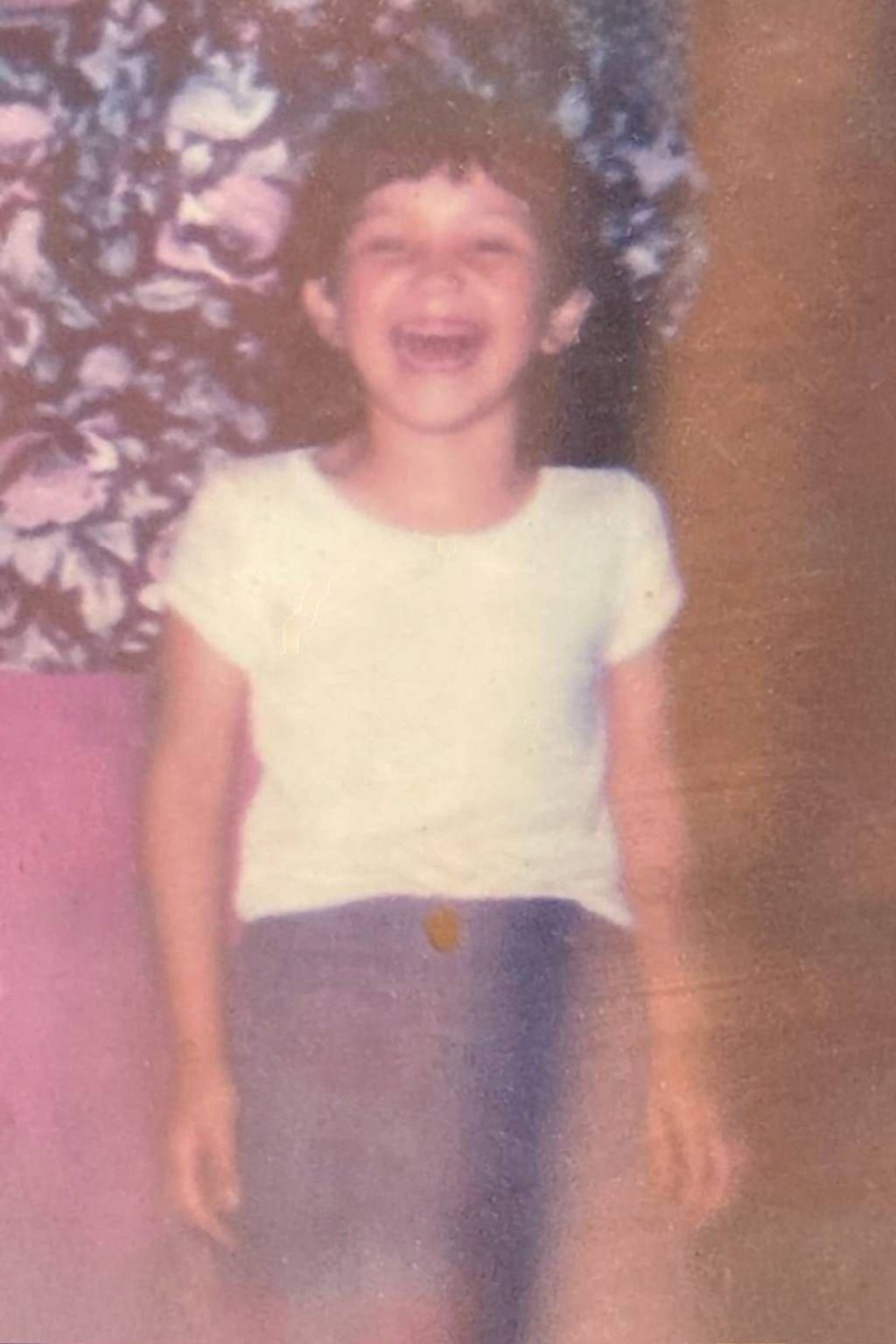 A young girl in a white shirt and shorts is laughing.
