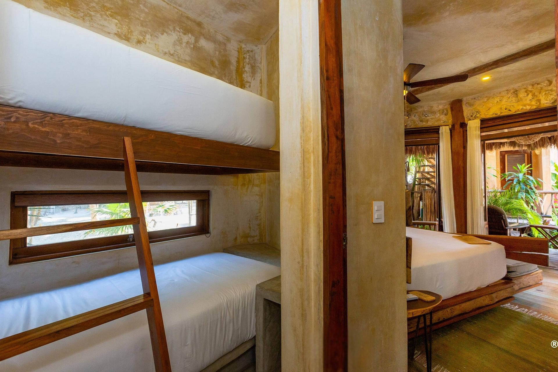 Bunk beds and a double bed in a room with a window to a balcony. Natural wood and concrete walls.