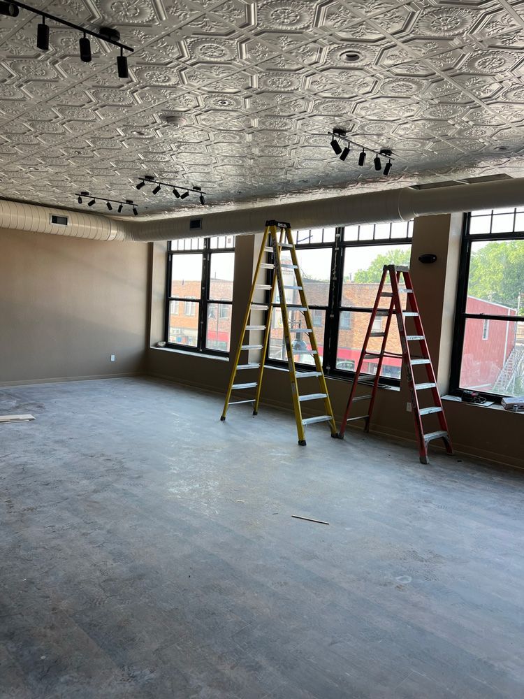 Two ladders are sitting in an empty room with lots of windows.