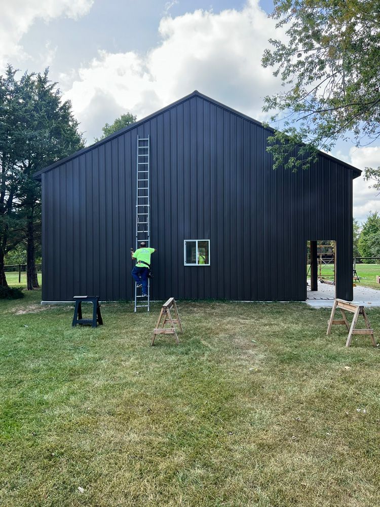 A man is standing on a ladder on the side of a black building.