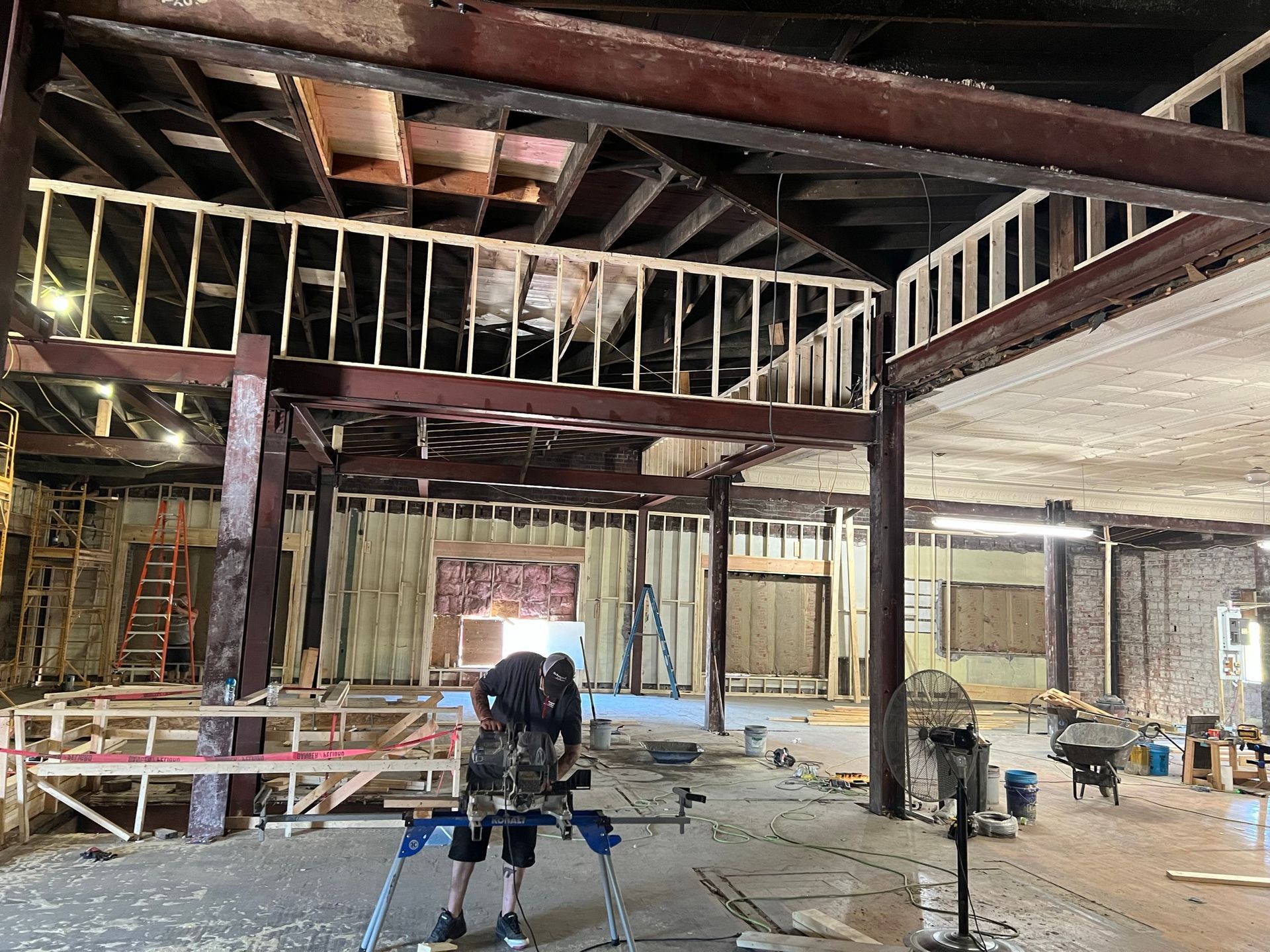 Interior construction site with workers, exposed beams, and a partially built mezzanine.