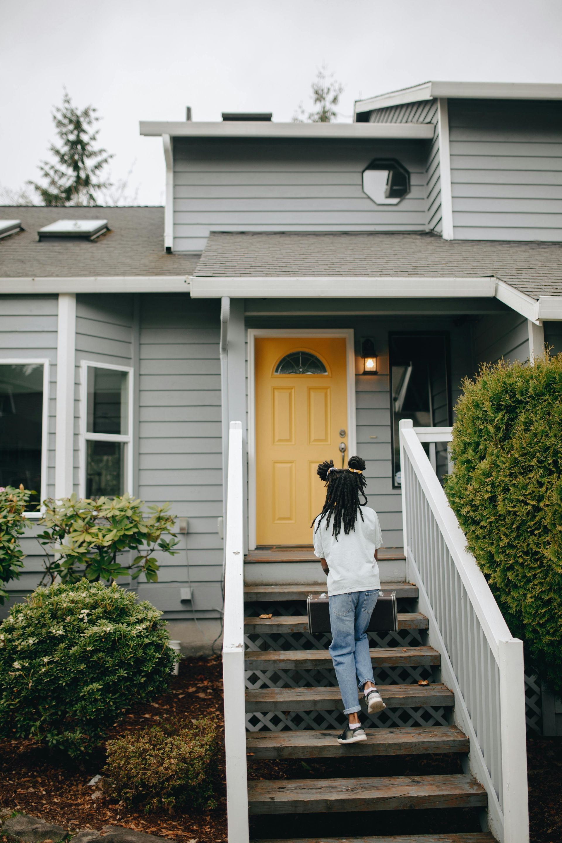 Girl climbs steps to a gray house with a yellow front door.