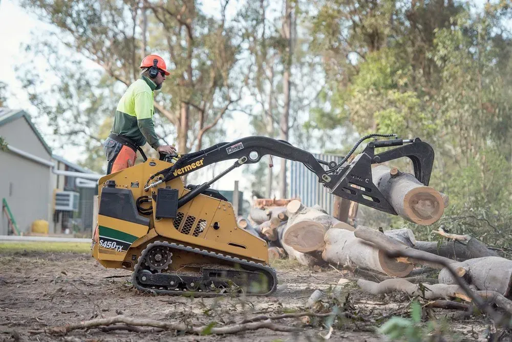 Man Operating a Yellow Skid Steer to Move Cut Logs Outdoors — Brown's Professional Tree Service in Widgee, QLD
