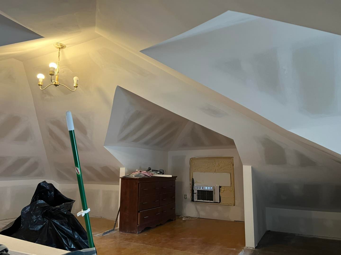 An attic with a dresser and a chandelier hanging from the ceiling