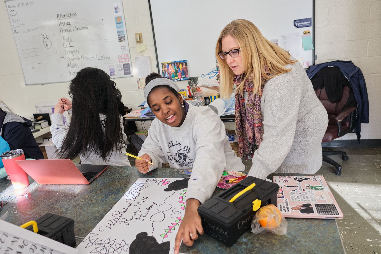 a woman is helping a girl with a project in a classroom