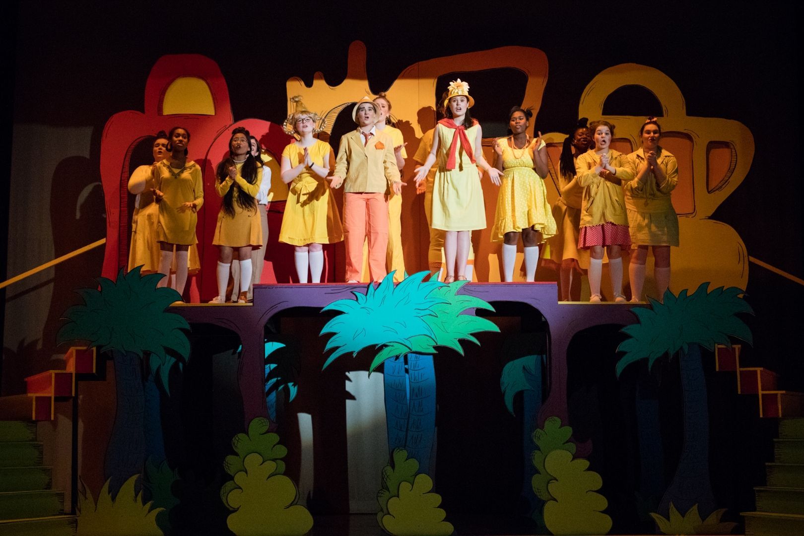 a group of children in yellow dresses stand on a stage