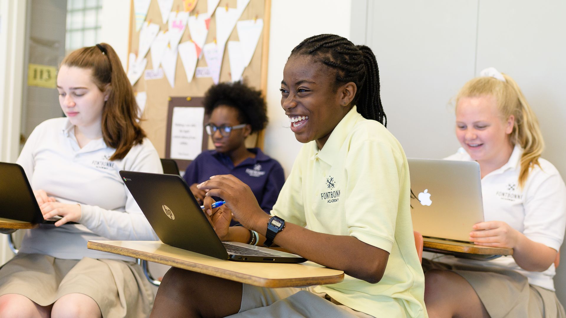 a group of students are sitting at desks using laptops