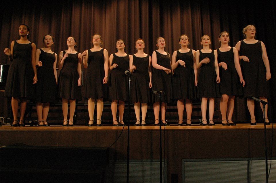 a group of women in black dresses are singing on a stage