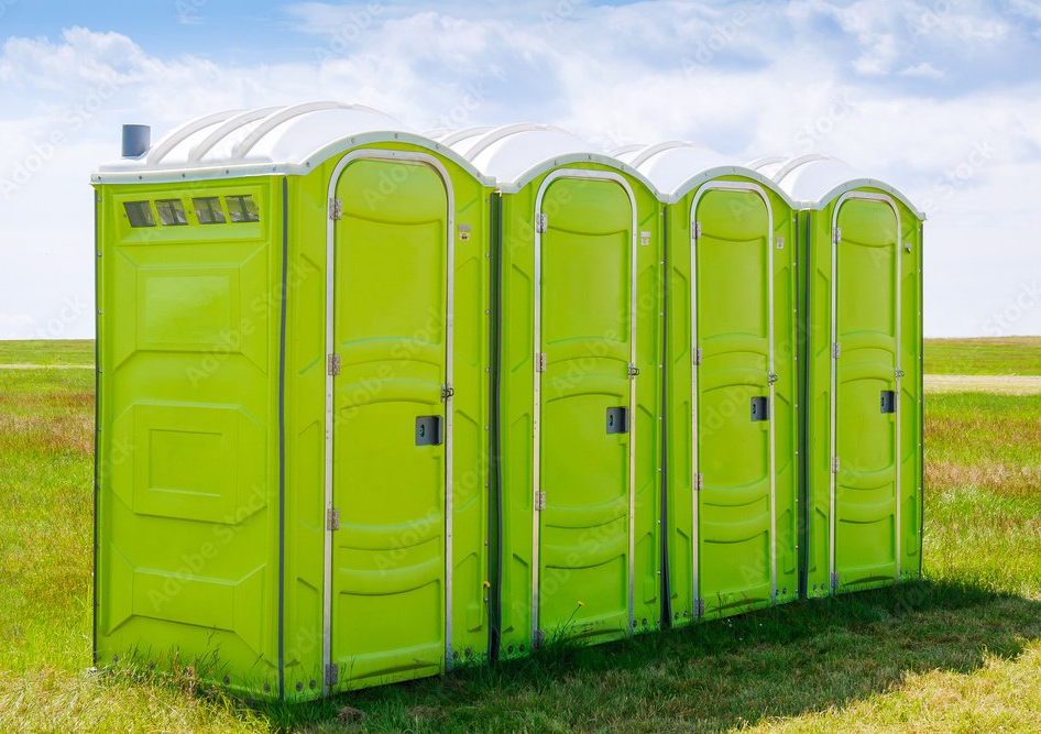 Quattro bagni chimici verdi in fila su un campo erboso.