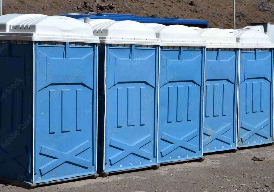 Bagni chimici blu e bianchi allineati sulla ghiaia.
