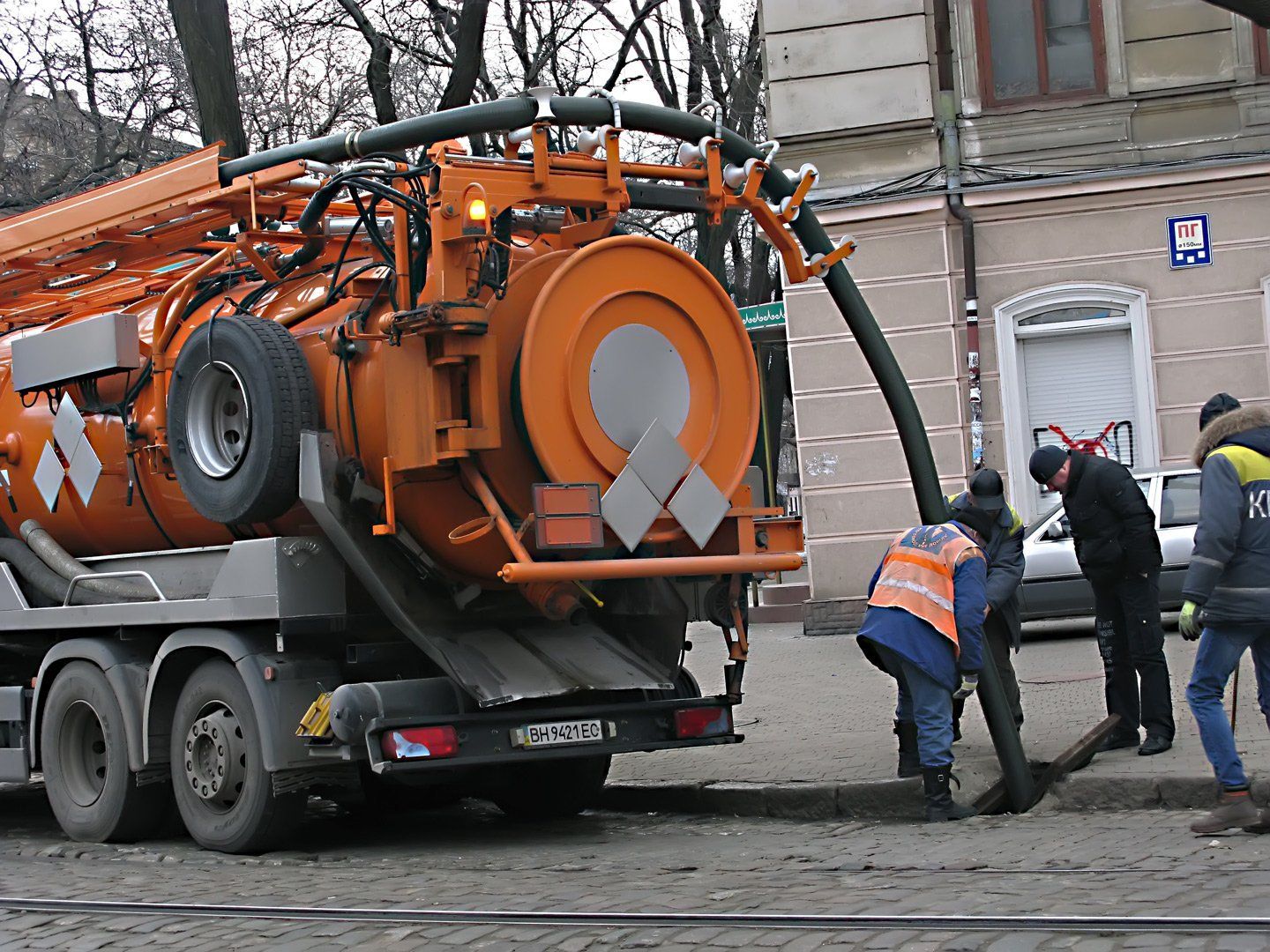 Autobotte arancione con operai che collegano un tubo a uno scarico stradale.