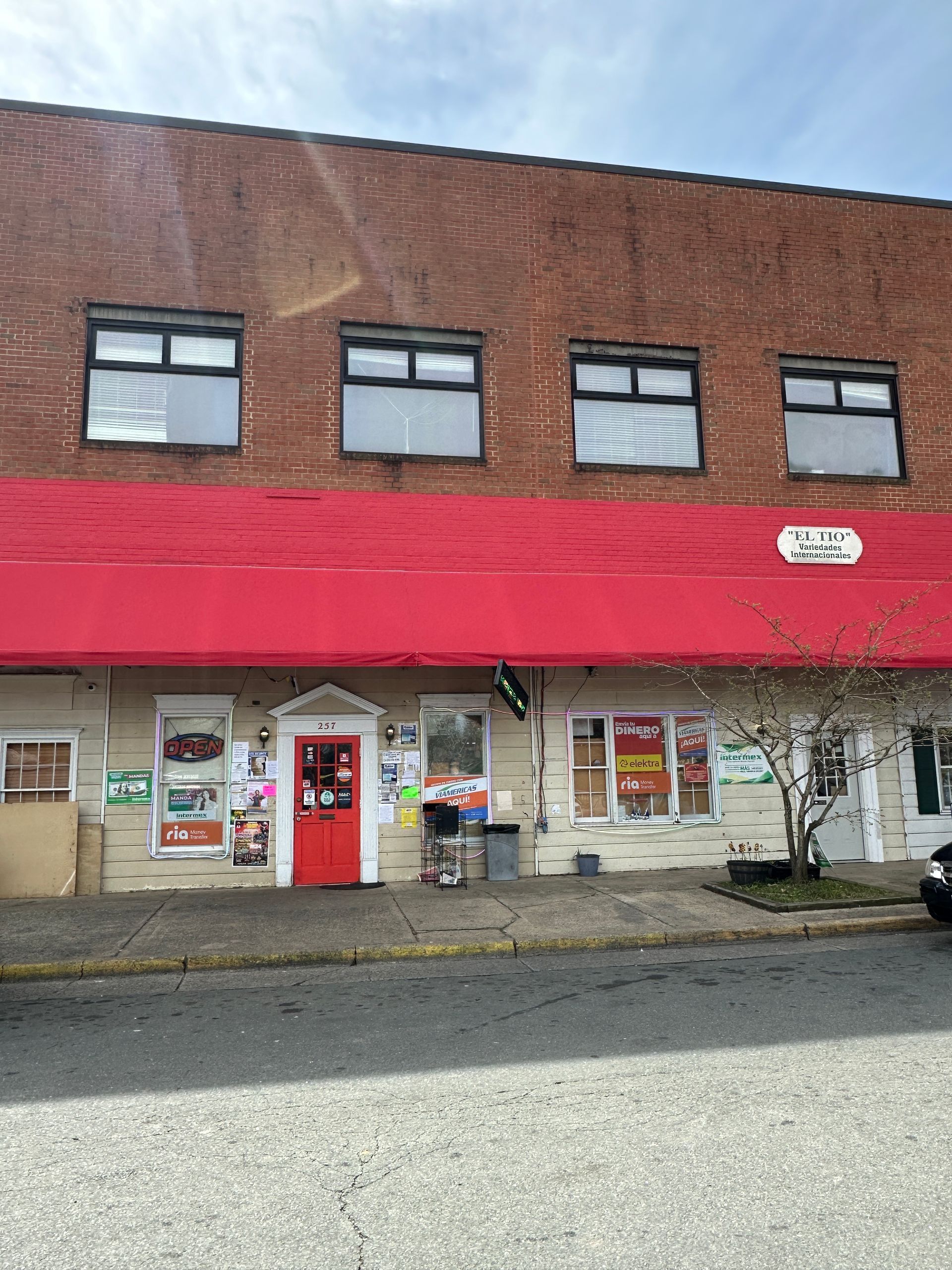 Red brick building with a red awning. Ground floor windows, a red door, and four windows above.