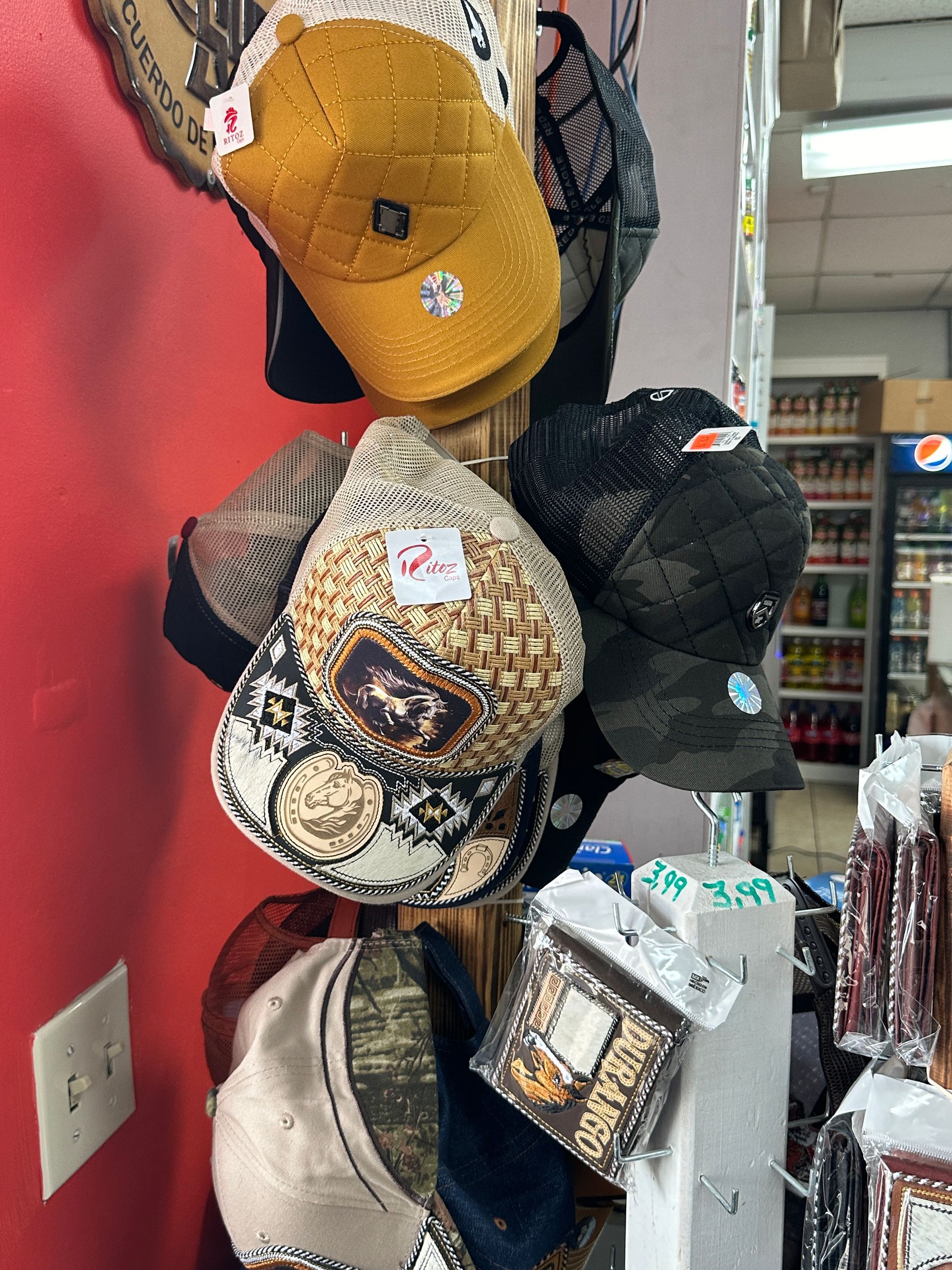 Hats of various colors and designs hanging on a display rack in a store, against a red wall.