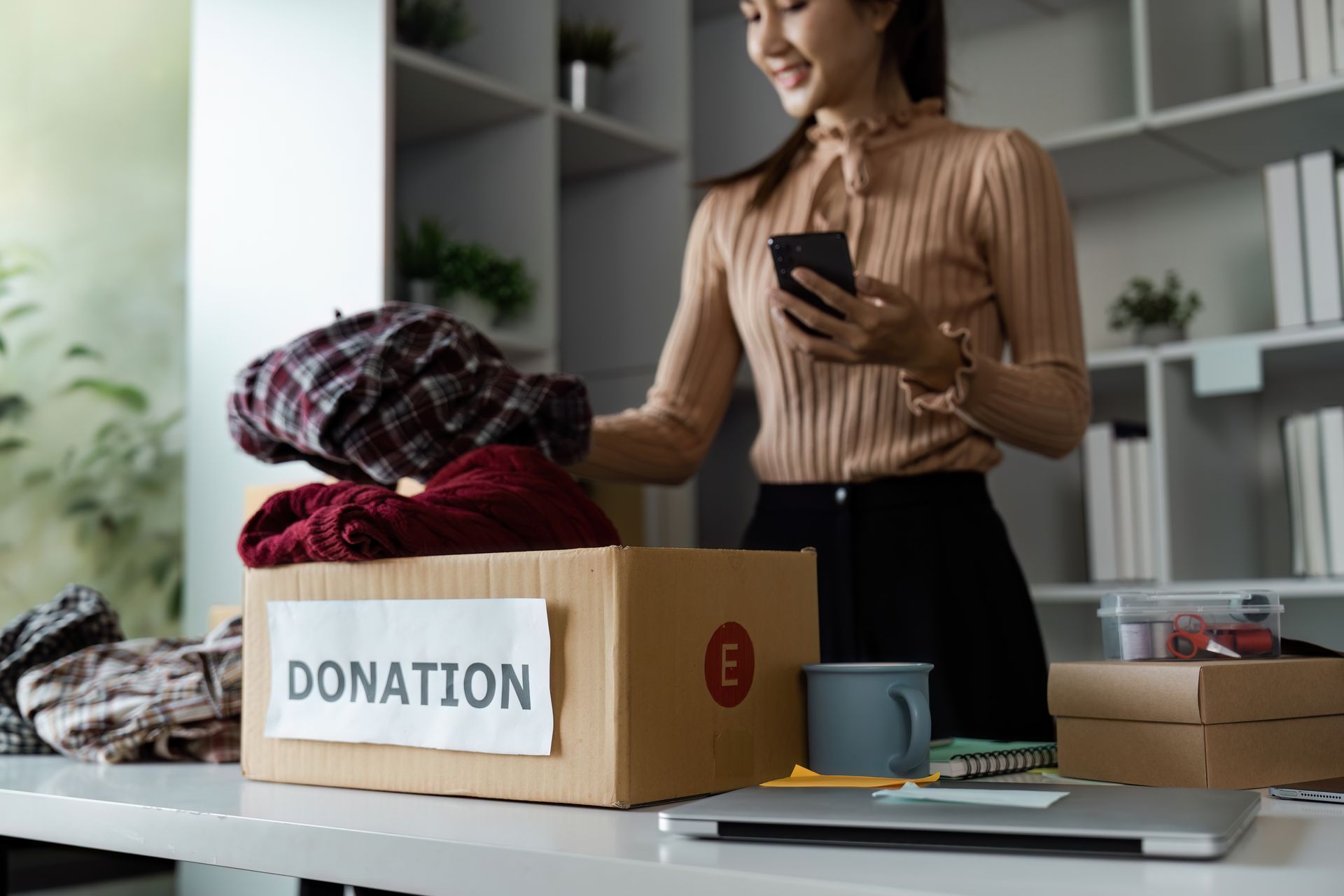 A woman is putting clothes in a donation box and looking at her phone.