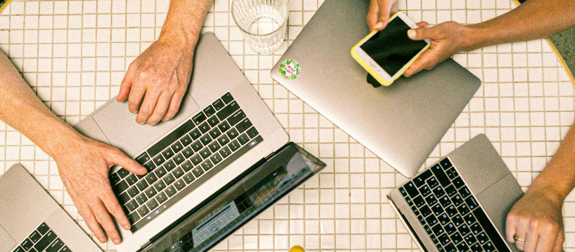 A group of people are sitting around a table using laptops and a cell phone.