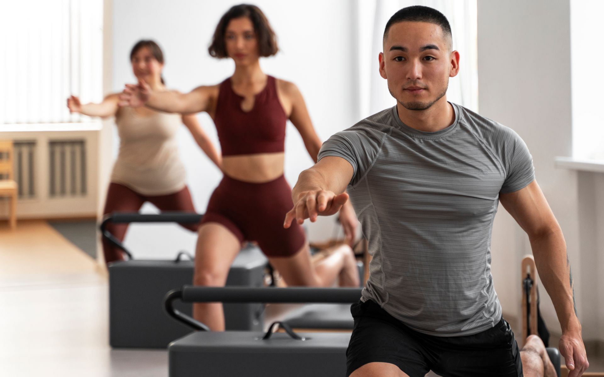 People doing a group workout in a bright studio, with a man in front leading a lunge exercise