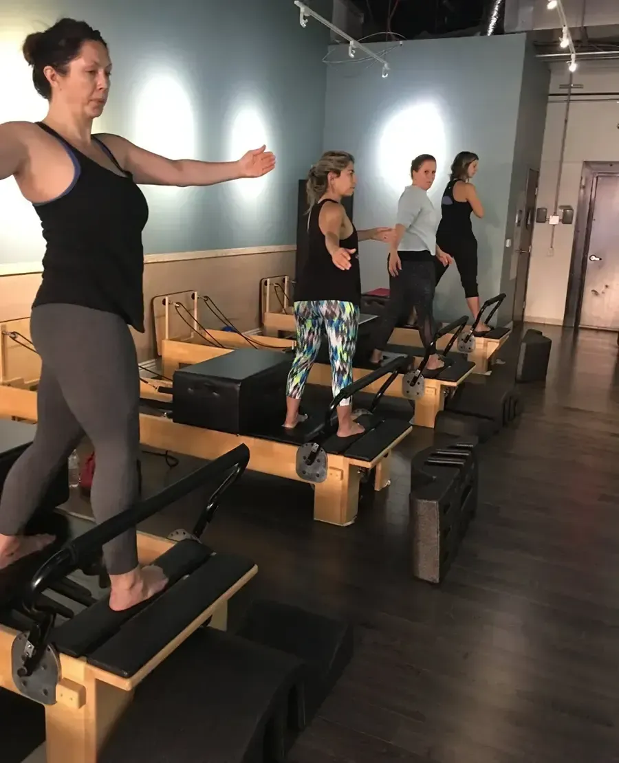 People exercising on Pilates reformers in a studio, facing mirrors and holding arm positions