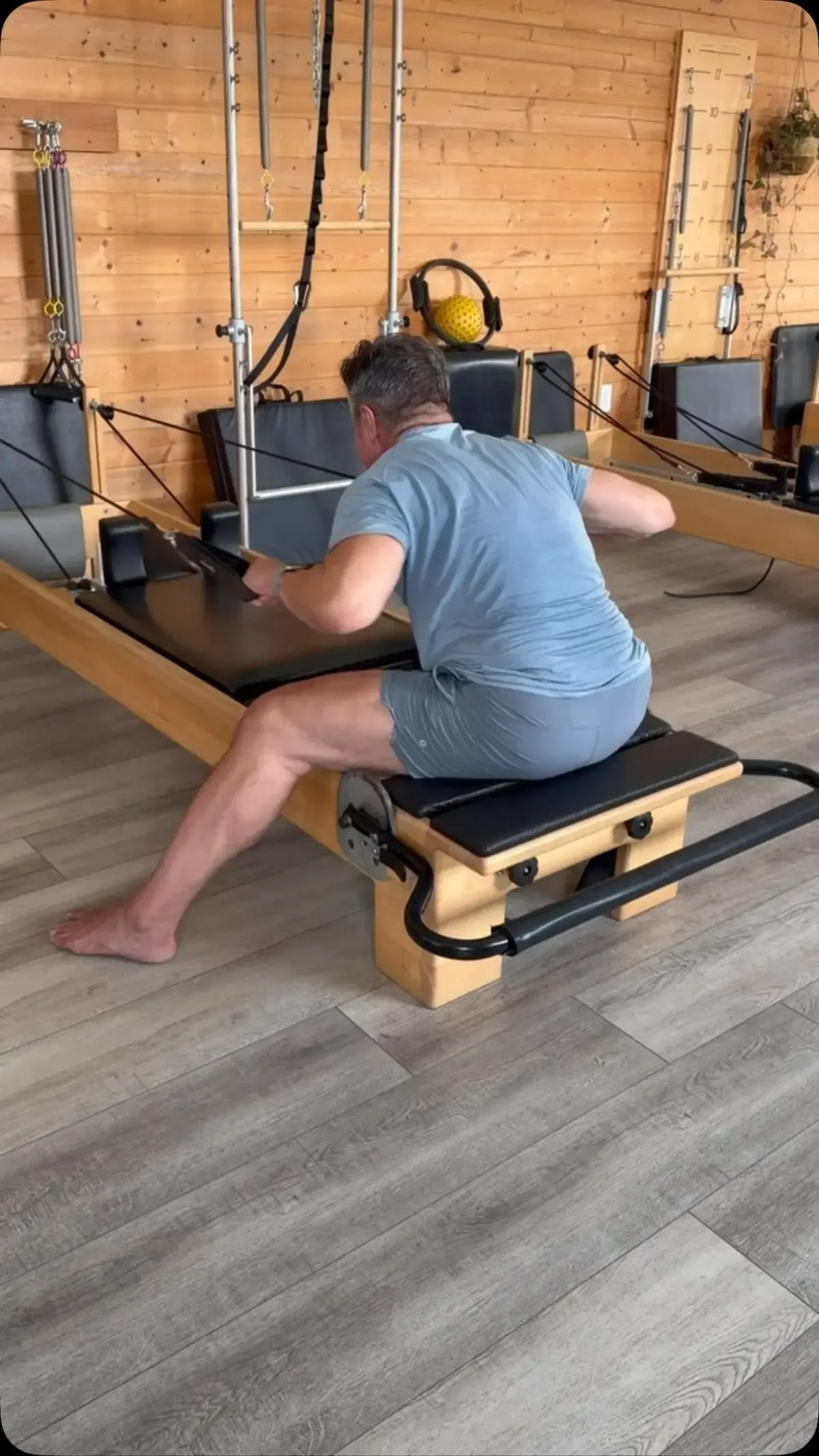 Two women doing Pilates side plank exercises on reformers in a bright studio