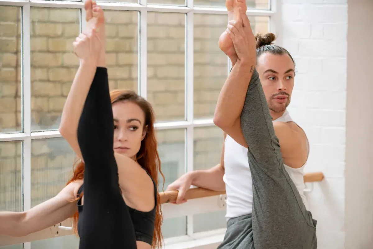 Two people exercising on reformer machines in a long studio hallway