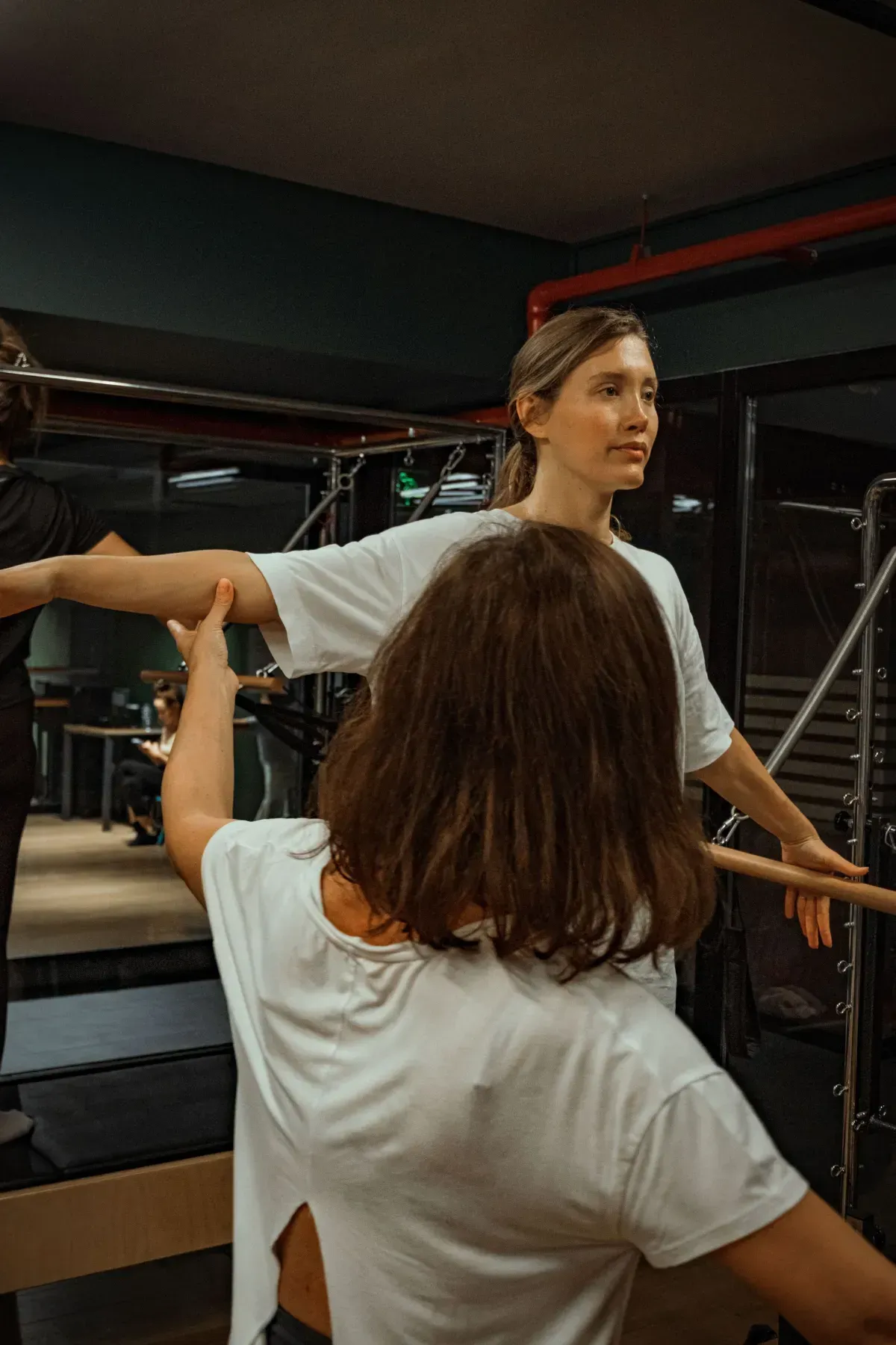 Woman balancing on one leg in a Pilates studio, holding a barre with outstretched arms.