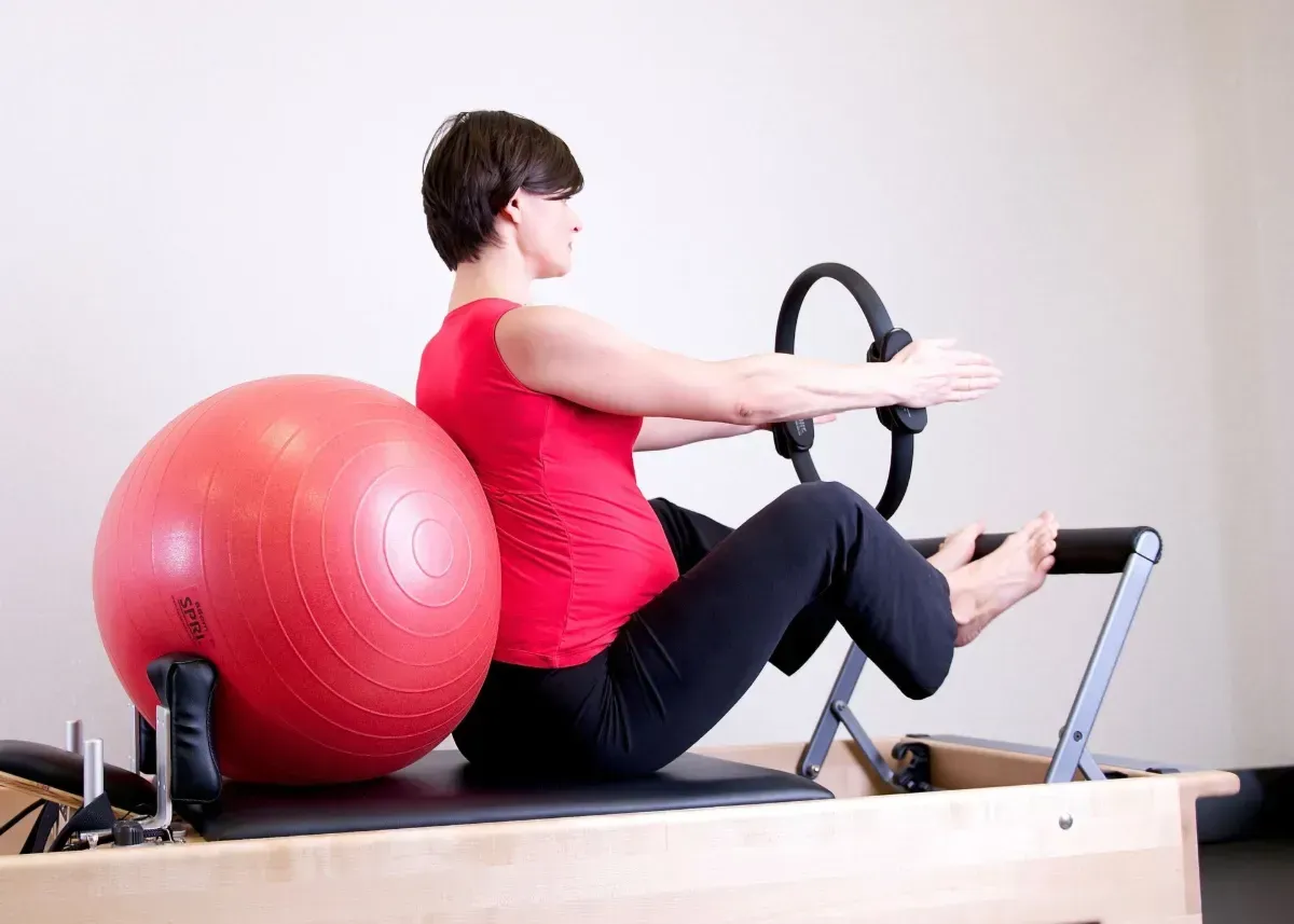 Two women doing Pilates side plank exercises on reformers in a bright studio