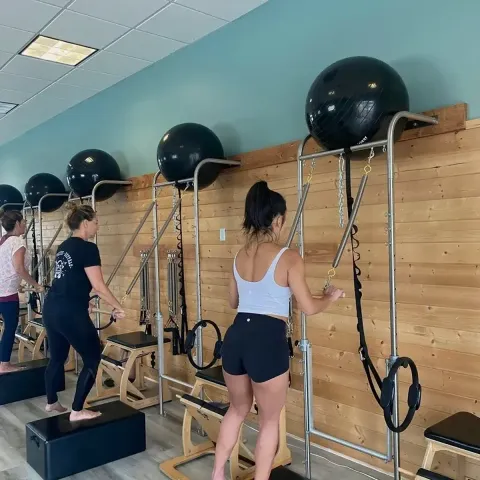 People exercising on Pilates reformers in a studio, using large exercise balls above the machines.