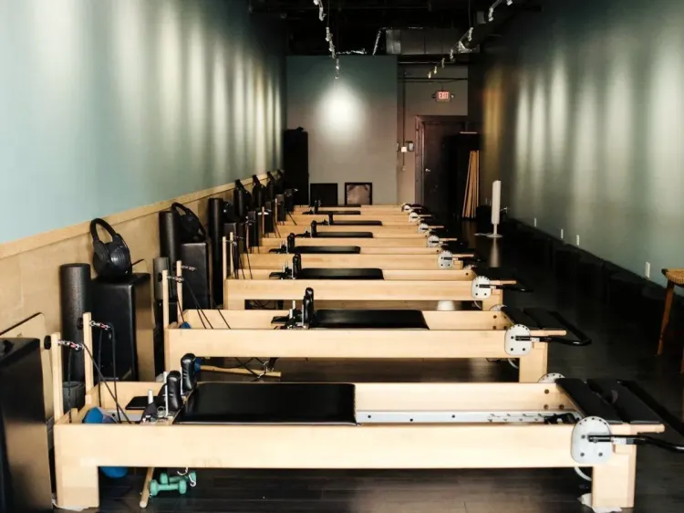 Long room with rows of reformer Pilates machines and wall mirrors on both sides