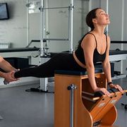 Trainer spotting a woman doing a Pilates leg extension on reformer equipment in a studio