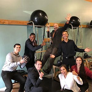Group posing in a dance studio with exercise balls and ballet bars, smiling and holding black balls