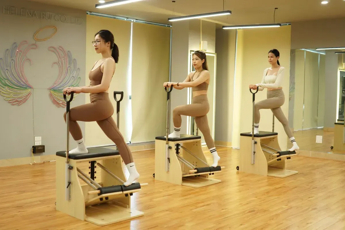 Three people using reformer machines in a mirrored Pilates studio