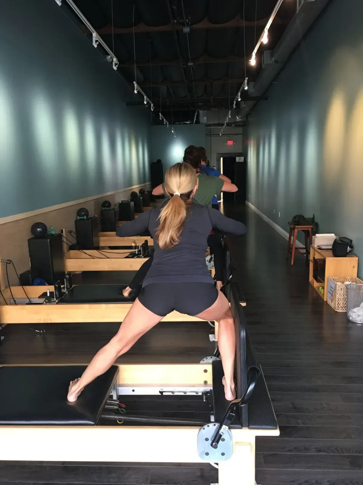 Two people exercising on reformer machines in a long studio hallway